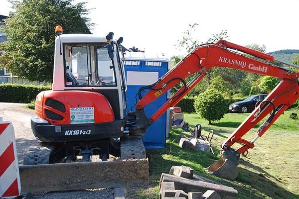 Gelber Kompaktbagger der Krasniqi GmbH beim Erdaushub an einem Hanggrundstück