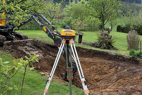 Tachymeter-Vermessung und Erdaushub mit Bagger vor Beginn des Teichbaus